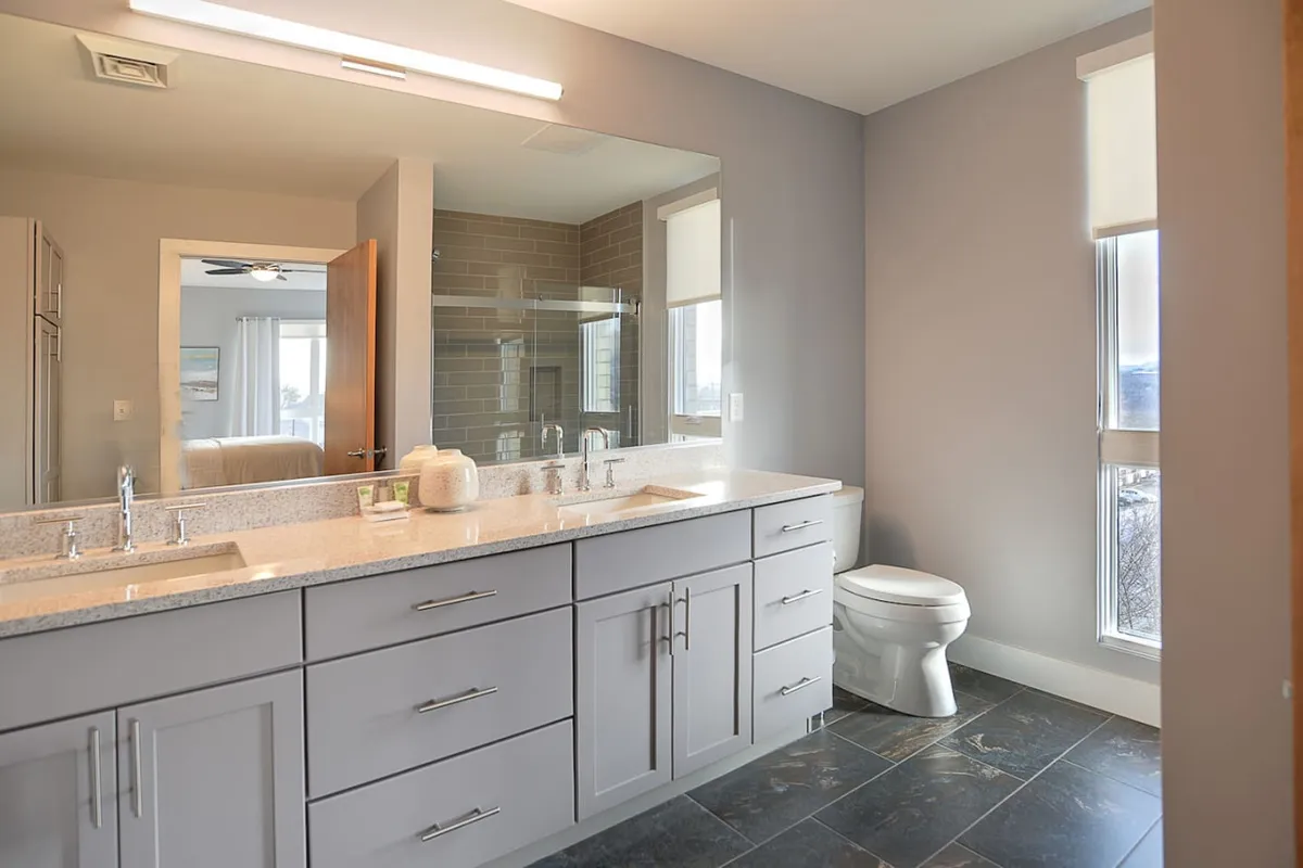 A modern ensuite bathroom with a double sink vanity, large mirror, glass shower, and a window providing natural light. The space is designed for both function and relaxation, featuring elegant finishes and ample room for daily routines.