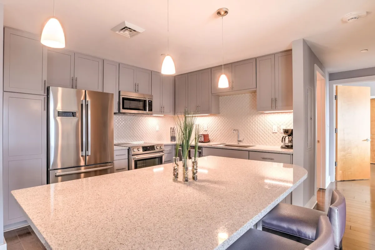 A modern kitchen with a generous island, gleaming stainless steel appliances, pendant lighting, and attractive backsplash tiles. The space is designed for cooking, entertaining, and enjoying meals together, with plenty of room for group activities.