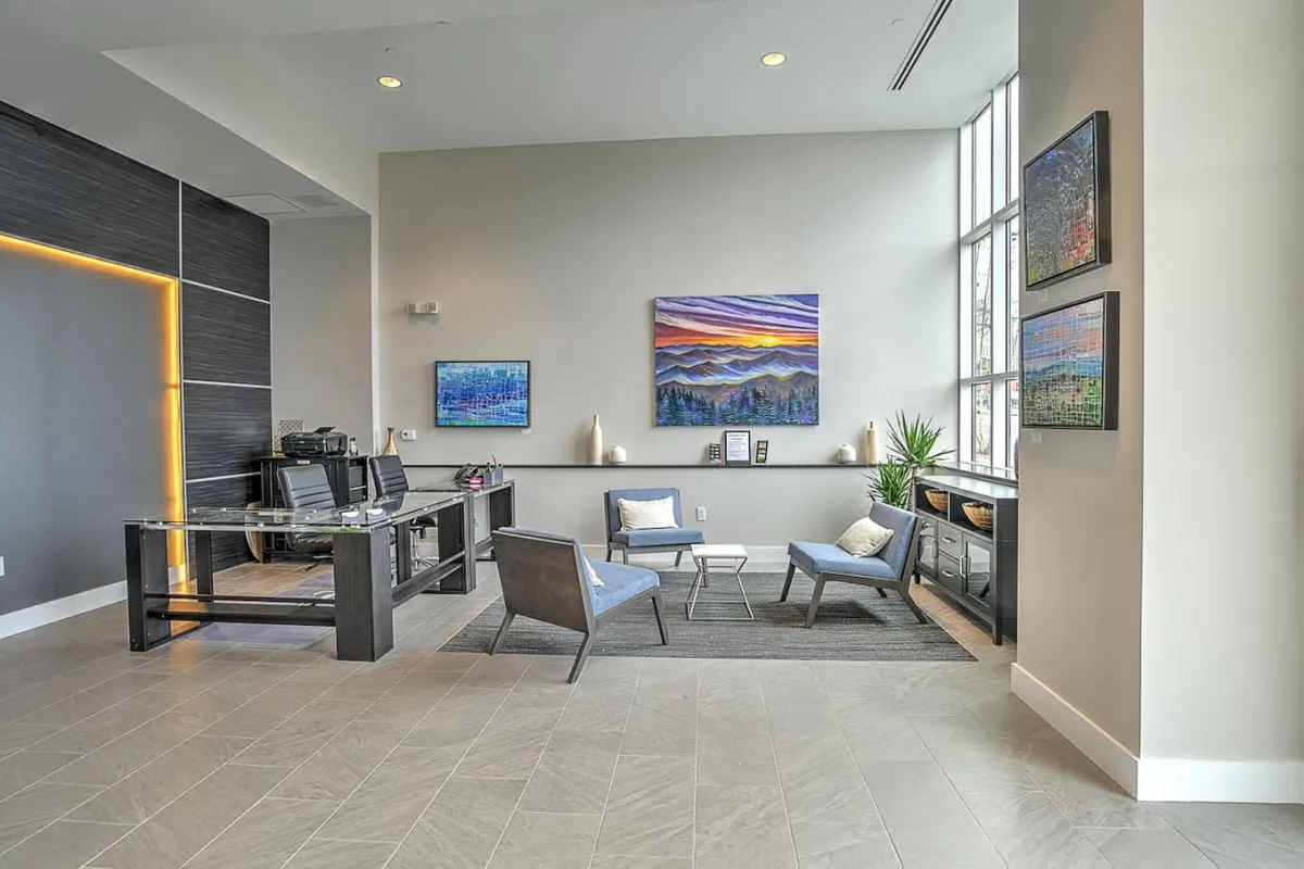 A sophisticated lobby or common area featuring contemporary artwork, modern furniture, and a work desk. The scene is calm and professional, suggesting a welcoming environment for guests and residents.