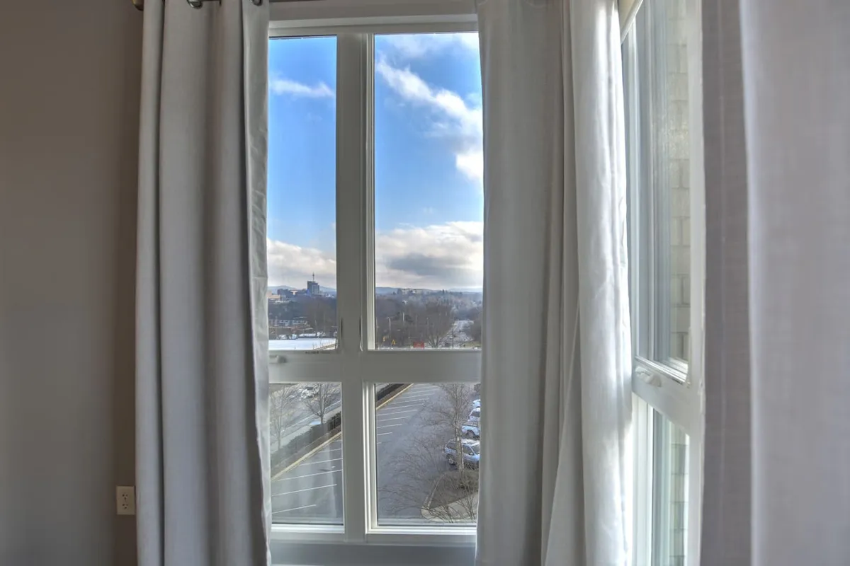This image captures a window with sheer curtains, framing a sky view, and is suffused with natural light. The scene evokes the feeling of starting the day with sunlight streaming in, possibly while sipping coffee and planning an adventure in the city.